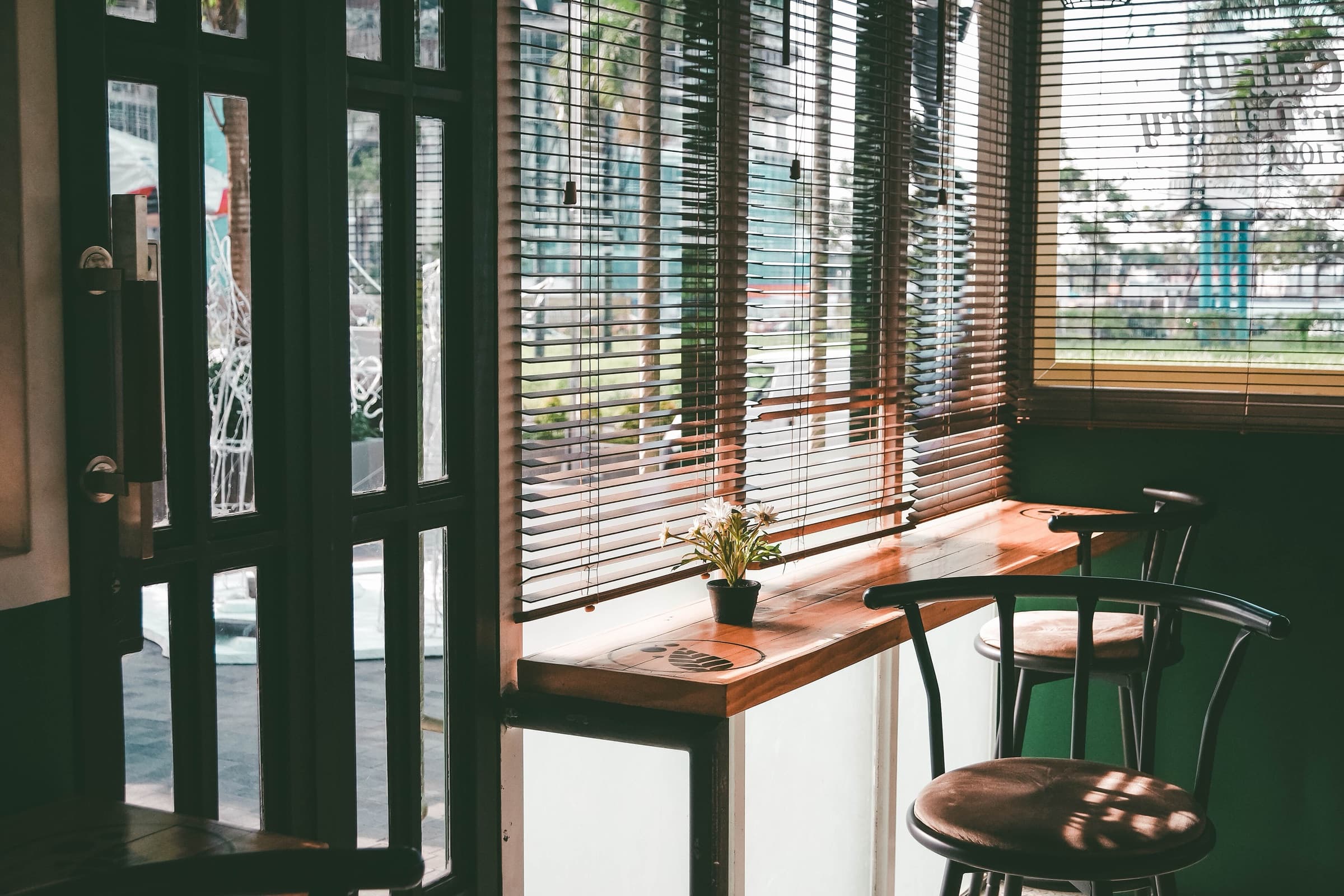Sunlight through wooden blinds in a green-framed cafe with palm trees outside